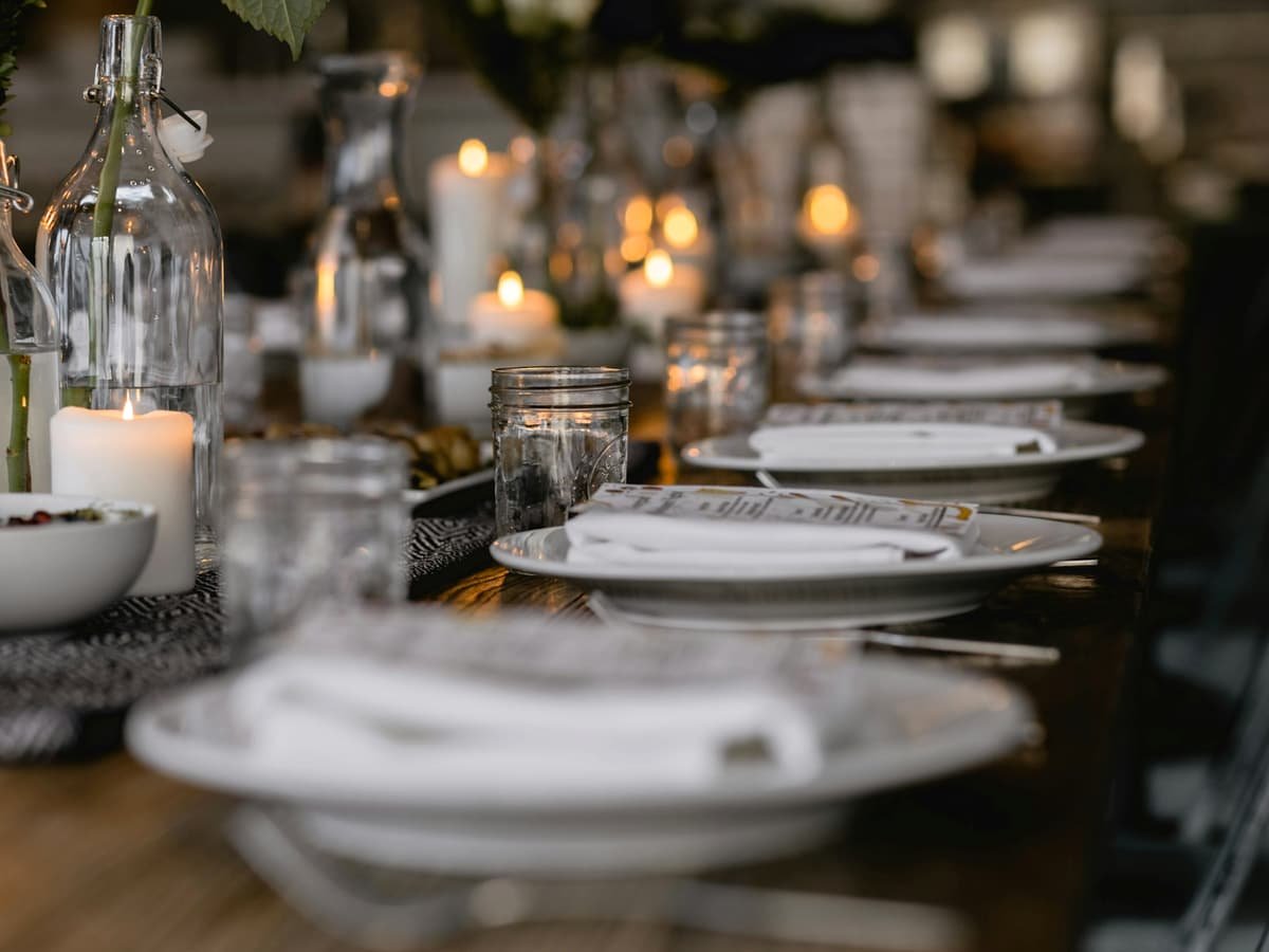 A long dining table set with white plates, candles, and glass bottles