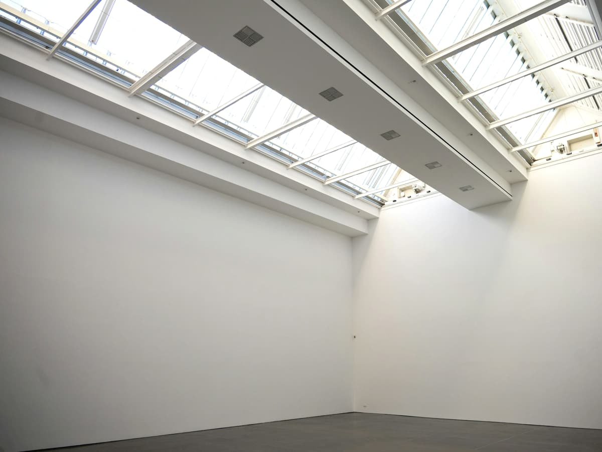 Empty white gallery room with skylights and concrete floor