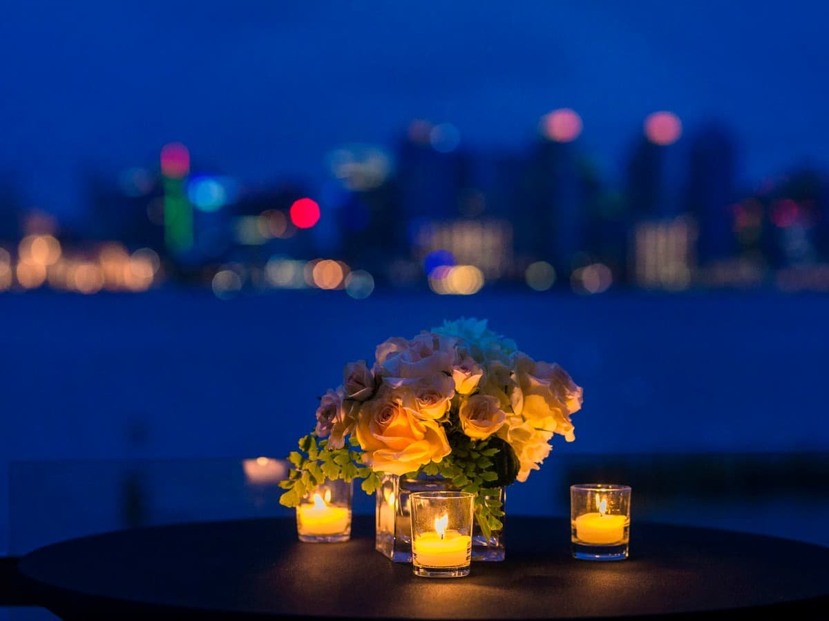 White rose bouquet in vase with three tealight candle votives on round brown wooden table