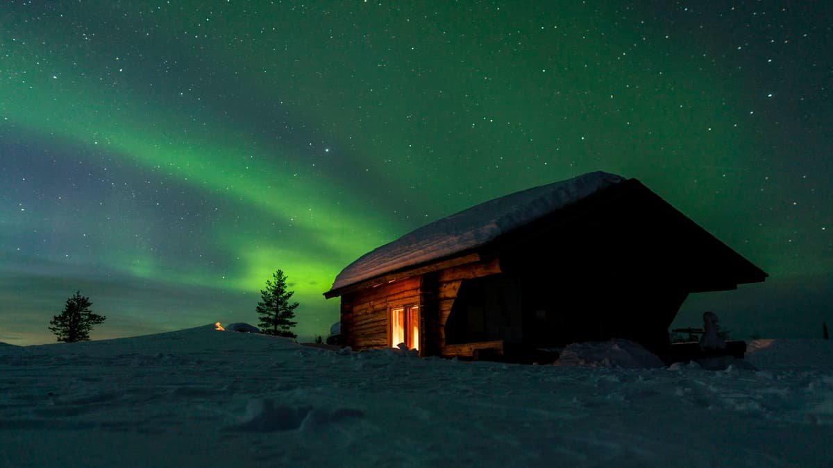 A cabin in the snow under a green aurora borealis
