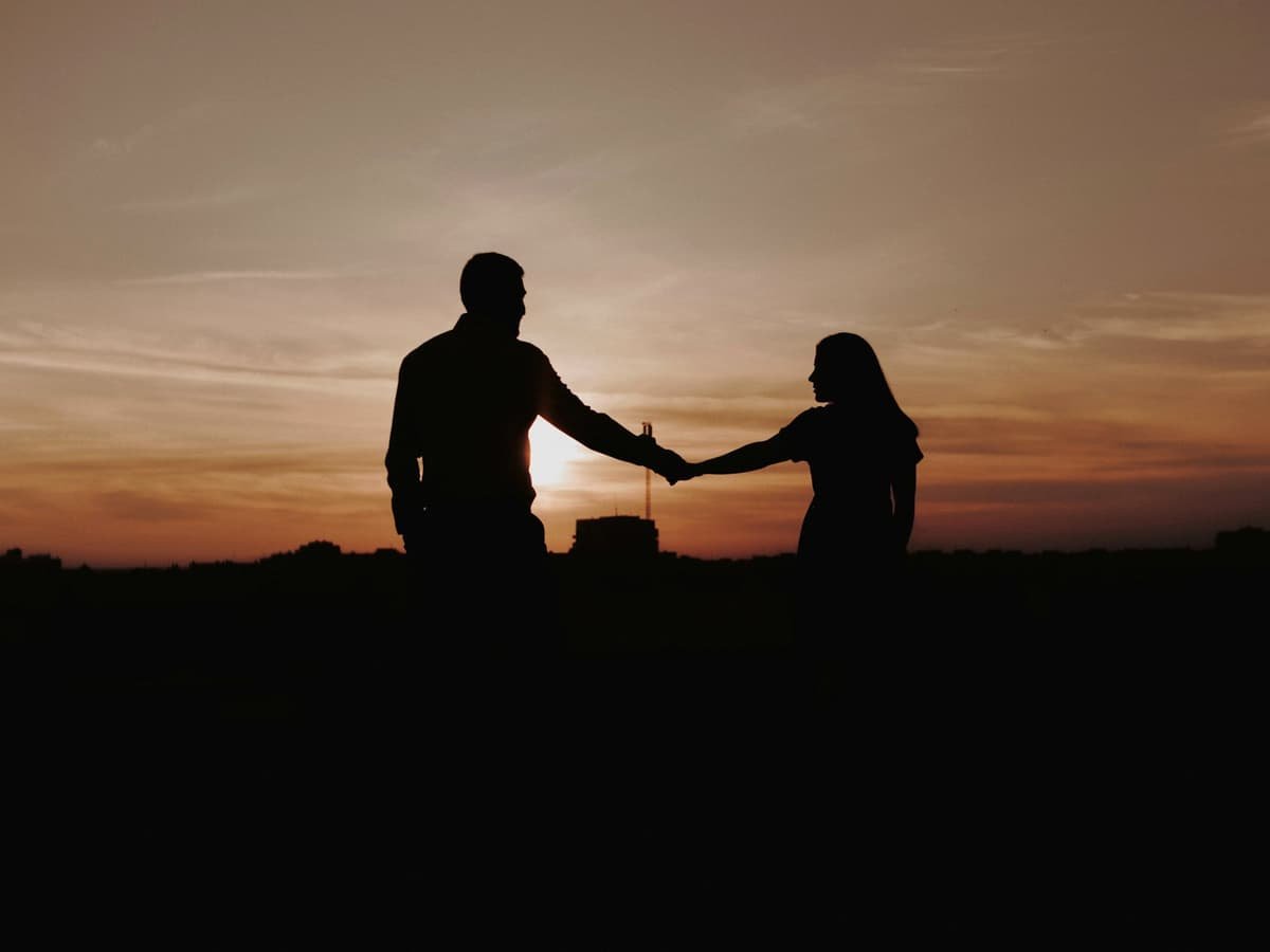 Silhouette of man and woman standing on ground during sunset