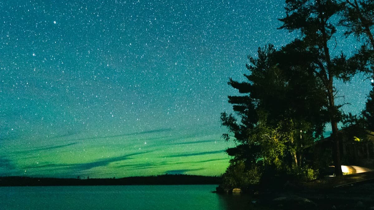 A green and blue sky filled with stars above a body of water