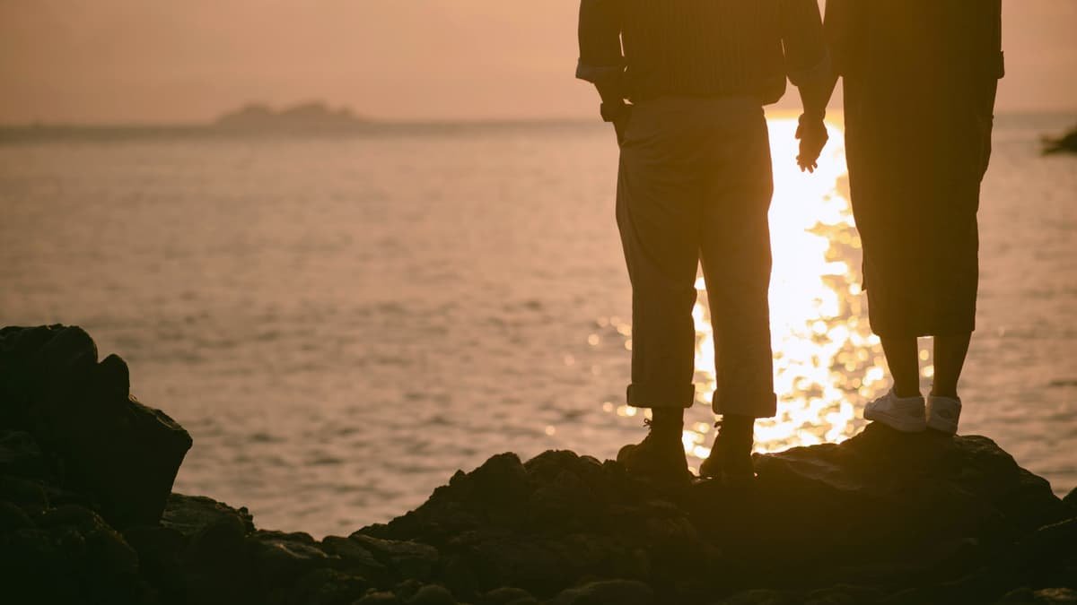 Two people in silhouette holding hands on a rocky shore at golden hour, date night in British Columbia