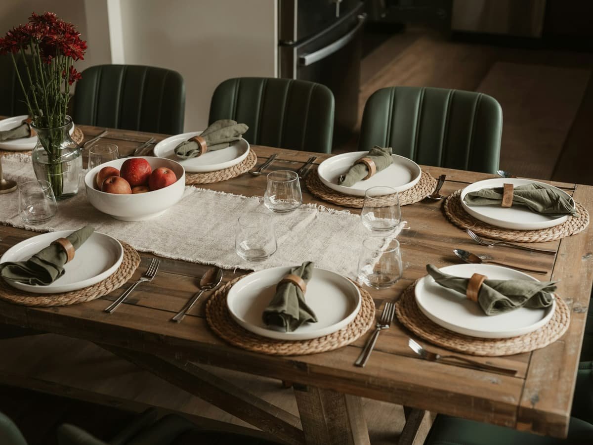 A wooden dining table set with white plates, green napkins, and red apples: date idea in New Brunswick