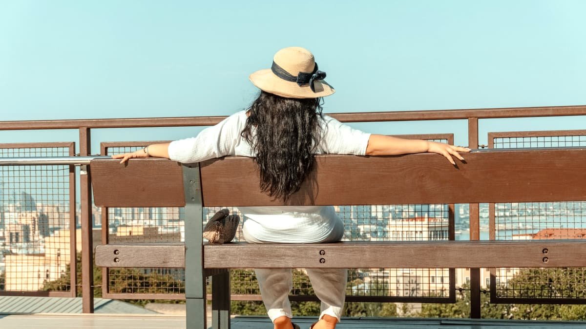 Woman in hat sits on bench overlooking city view, date night in Saskatchewan